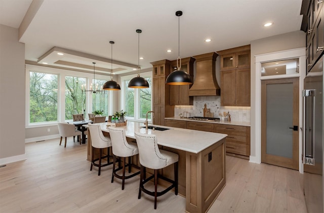 kitchen featuring custom range hood, a sink, light wood-style floors, and brown cabinetry