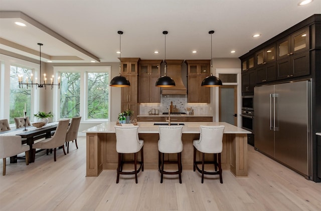 kitchen featuring custom range hood, light wood-style flooring, an inviting chandelier, and stainless steel appliances