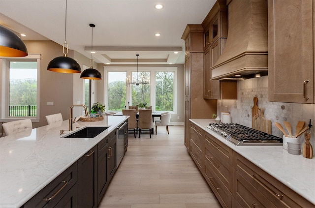 kitchen featuring a sink, light wood-style flooring, premium range hood, stainless steel appliances, and decorative backsplash
