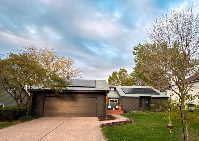 mid-century home featuring a garage, a front lawn, roof with shingles, roof mounted solar panels, and driveway