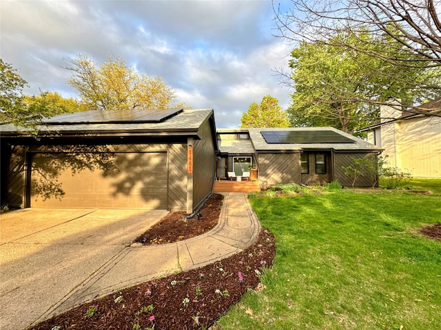 mid-century home featuring driveway, roof mounted solar panels, a front yard, and a garage