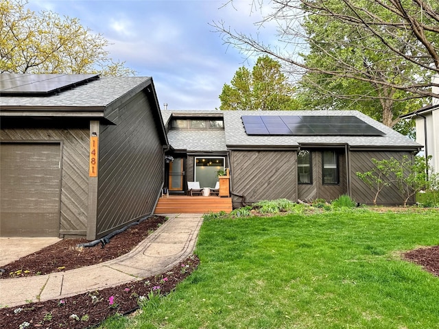 rear view of house featuring a yard, solar panels, and roof with shingles