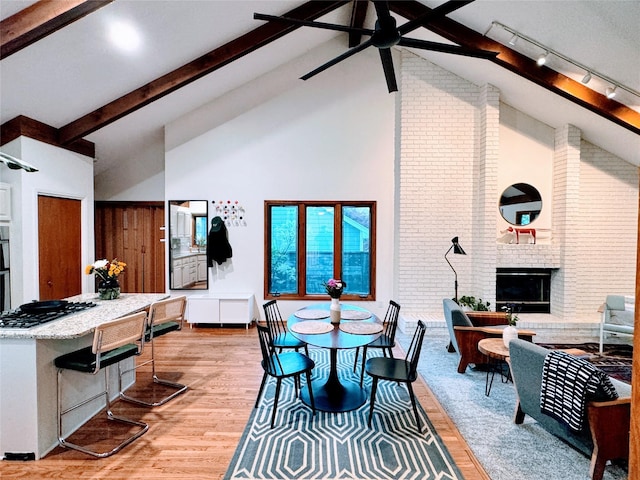 dining room featuring track lighting, beam ceiling, high vaulted ceiling, and light wood-type flooring