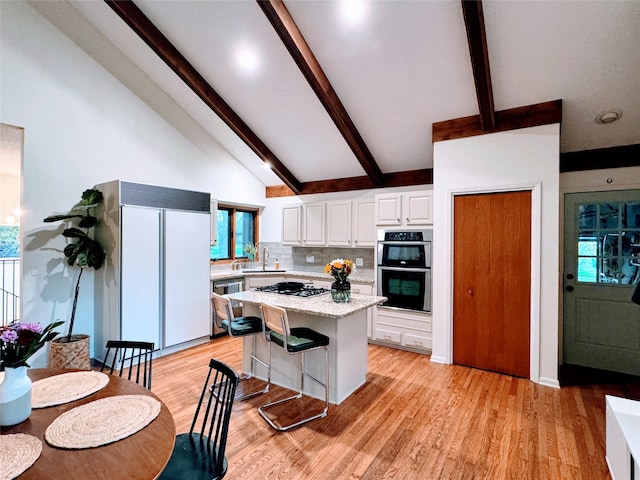 kitchen with decorative backsplash, beamed ceiling, white cabinets, a sink, and appliances with stainless steel finishes