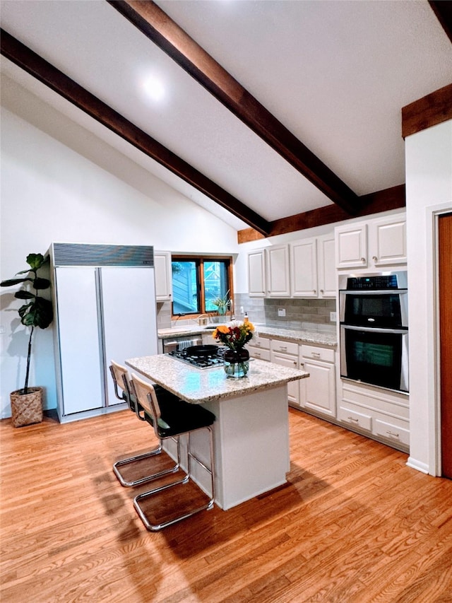 kitchen with white cabinets, appliances with stainless steel finishes, lofted ceiling with beams, backsplash, and a kitchen island
