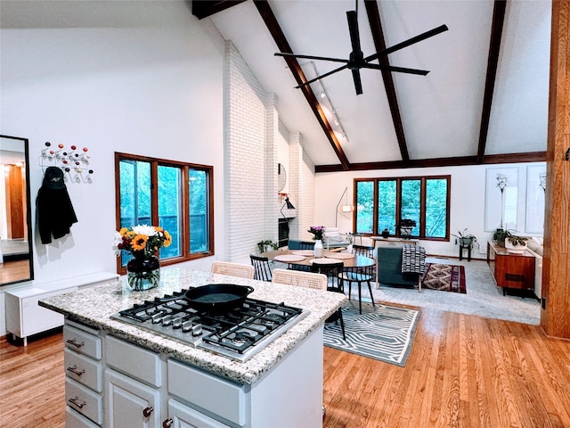 kitchen featuring beam ceiling, high vaulted ceiling, a ceiling fan, open floor plan, and stainless steel gas stovetop