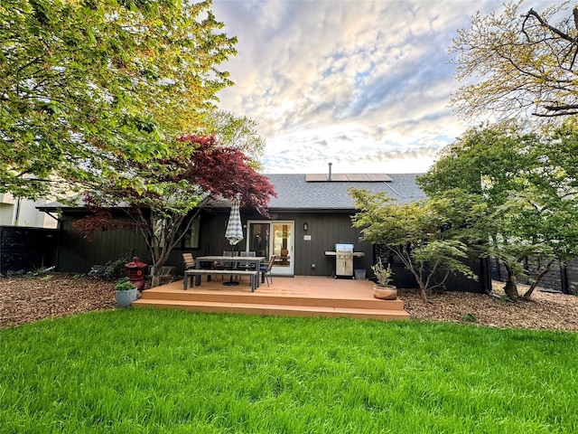 back of property with a yard, a deck, solar panels, and a shingled roof