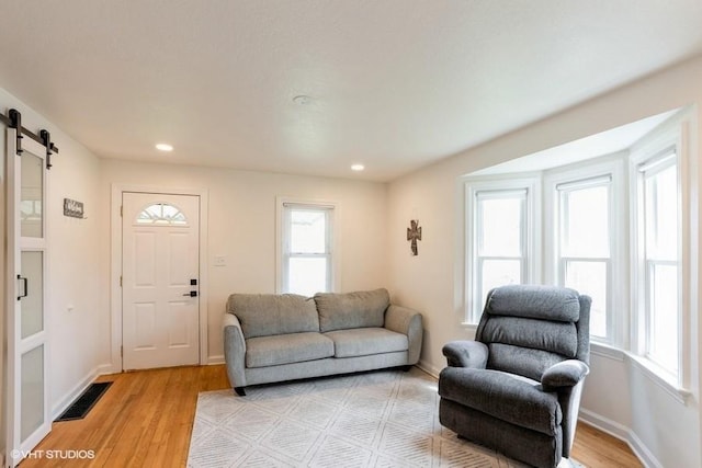 living area with a wealth of natural light, light wood-type flooring, a barn door, and visible vents