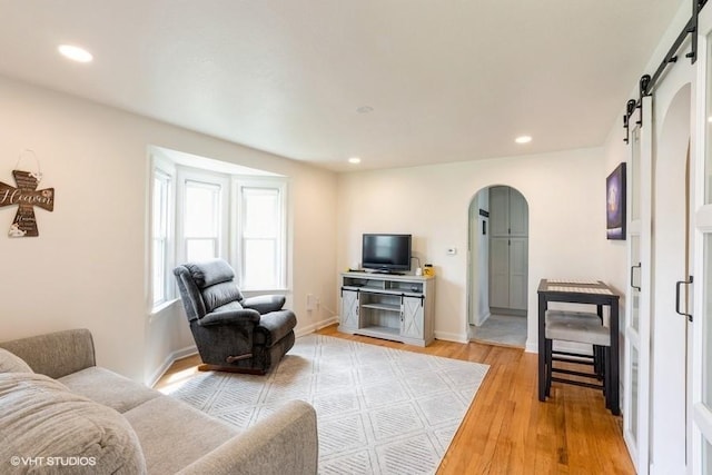 living area with a barn door, arched walkways, light wood-style flooring, recessed lighting, and baseboards