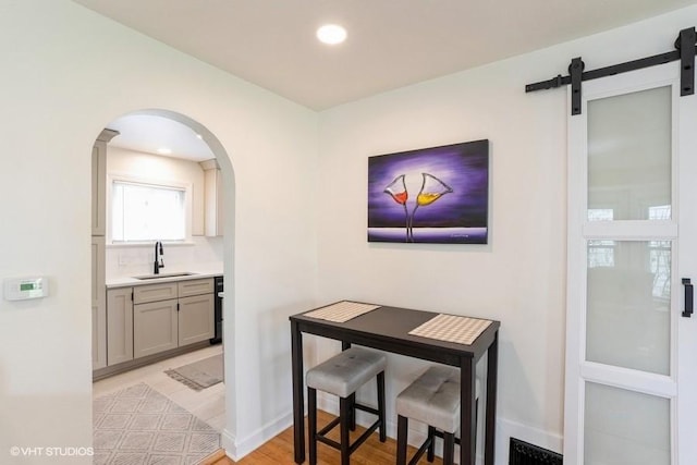 dining space with a barn door, light wood-style floors, arched walkways, recessed lighting, and baseboards