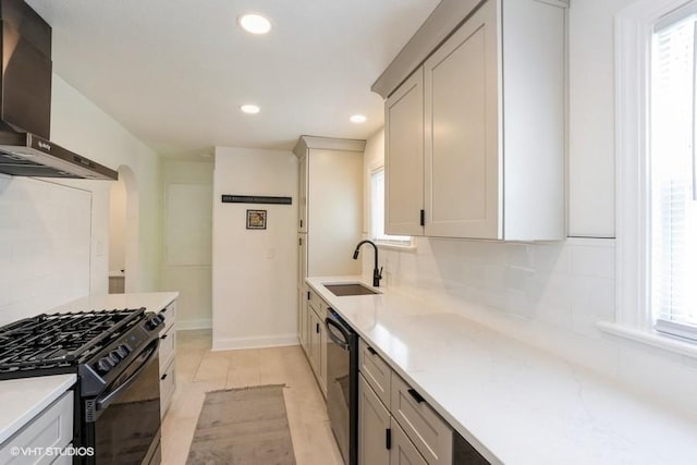 kitchen featuring plenty of natural light, a sink, black appliances, and wall chimney range hood