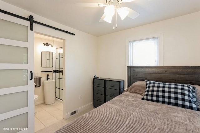 bedroom featuring a ceiling fan, tile patterned flooring, a barn door, baseboards, and ensuite bathroom