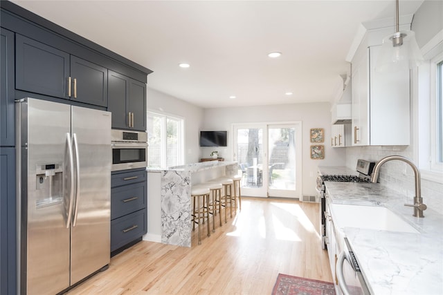 kitchen with light wood-style floors, appliances with stainless steel finishes, a kitchen breakfast bar, and a sink