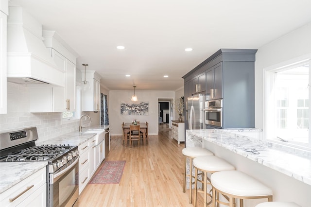 kitchen featuring appliances with stainless steel finishes, a sink, light wood-style floors, a kitchen bar, and custom exhaust hood