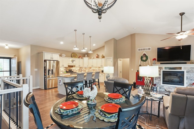 2006 NE 16th St, Ankeny, IA 50021 - dining space featuring a fireplace, light wood-style floors, a ceiling fan, lofted ceiling, and visible vents