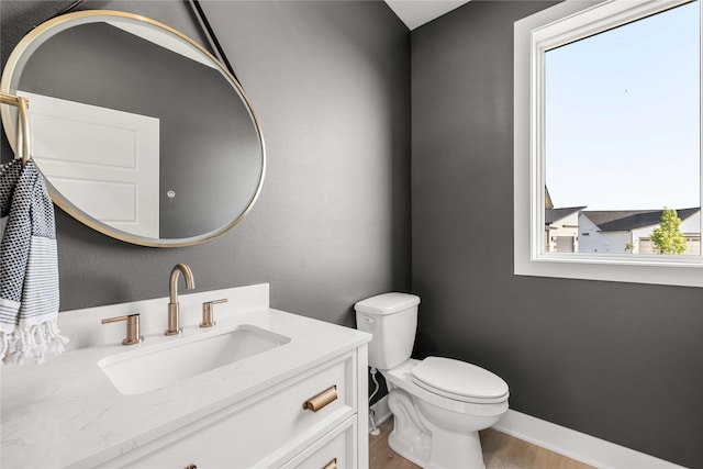 half bath with vanity, baseboards, wood finished floors, and toilet