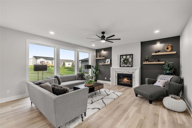 living room featuring baseboards, a high end fireplace, light wood-style flooring, and ceiling fan