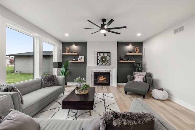 living area featuring light wood finished floors, a premium fireplace, a ceiling fan, baseboards, and visible vents