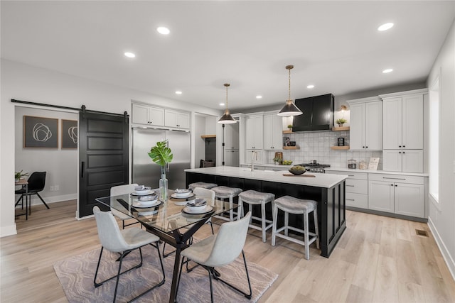 dining room with recessed lighting, baseboards, a barn door, and light wood-type flooring