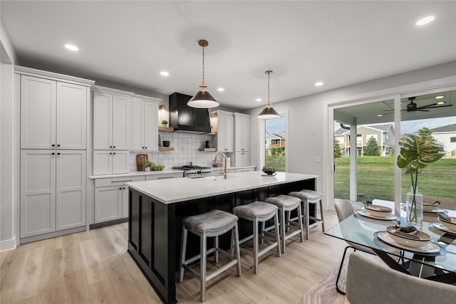 kitchen with a breakfast bar, light countertops, wall chimney exhaust hood, light wood-type flooring, and a center island with sink