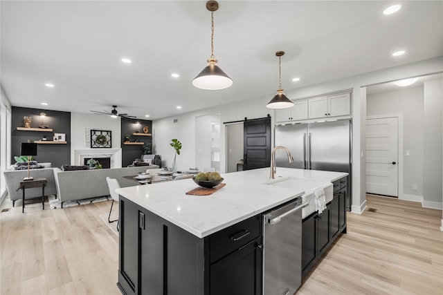kitchen with a ceiling fan, light wood-type flooring, a barn door, a sink, and stainless steel appliances