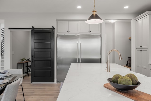 kitchen with a barn door, recessed lighting, light wood-type flooring, pendant lighting, and stainless steel built in refrigerator