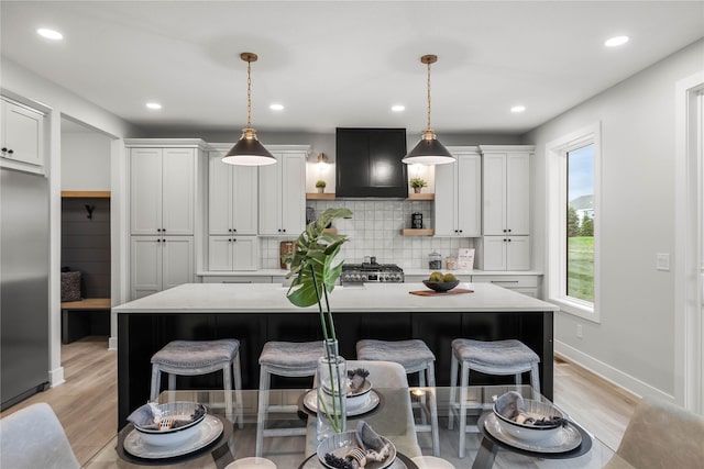 kitchen featuring exhaust hood, a kitchen breakfast bar, built in fridge, and light countertops