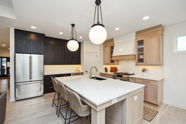 kitchen with high quality appliances, a center island with sink, a sink, custom exhaust hood, and light wood finished floors