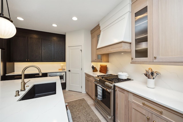kitchen featuring stainless steel gas range oven, a sink, light stone counters, custom exhaust hood, and glass insert cabinets