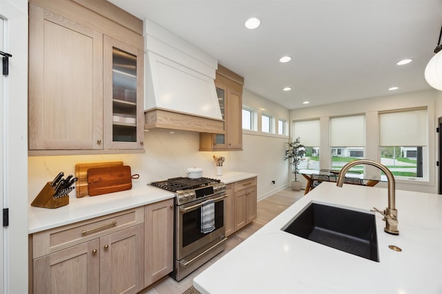 kitchen with a sink, light countertops, custom exhaust hood, stainless steel range with gas cooktop, and light wood-style floors