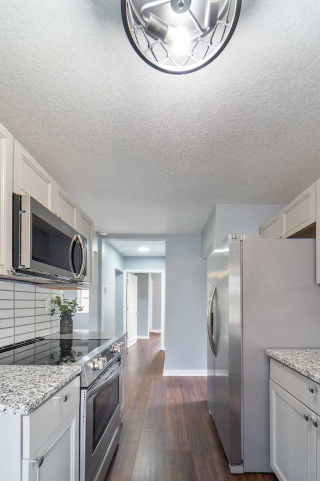 kitchen featuring baseboards, light stone countertops, stainless steel appliances, and dark wood-style flooring