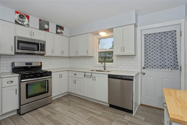 3924 55th St, Des Moines, IA 50310 - kitchen featuring appliances with stainless steel finishes, a sink, light wood-style floors, tasteful backsplash, and white cabinetry