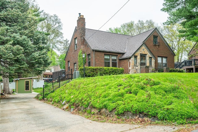 english style home featuring brick siding, central AC, an outdoor structure, a storage unit, and a shingled roof