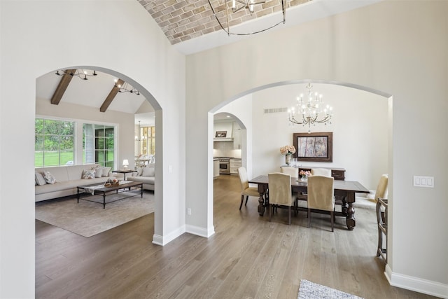 dining space with an inviting chandelier, high vaulted ceiling, and wood finished floors