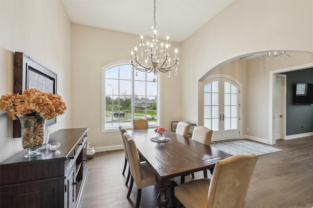 dining area featuring wood finished floors, baseboards, french doors, arched walkways, and a notable chandelier