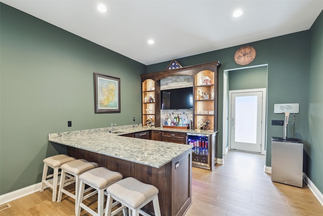 kitchen featuring open shelves, a sink, light wood finished floors, a peninsula, and wine cooler