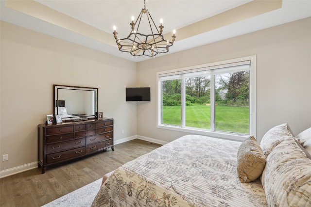 bedroom featuring an inviting chandelier, baseboards, wood finished floors, and a raised ceiling