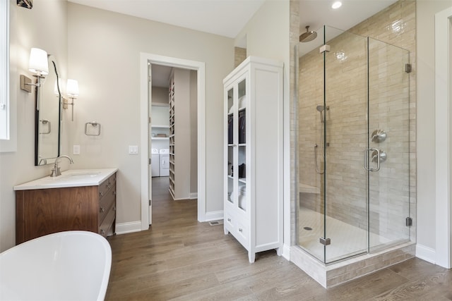 full bathroom with a freestanding bath, a walk in closet, vanity, wood finished floors, and a stall shower