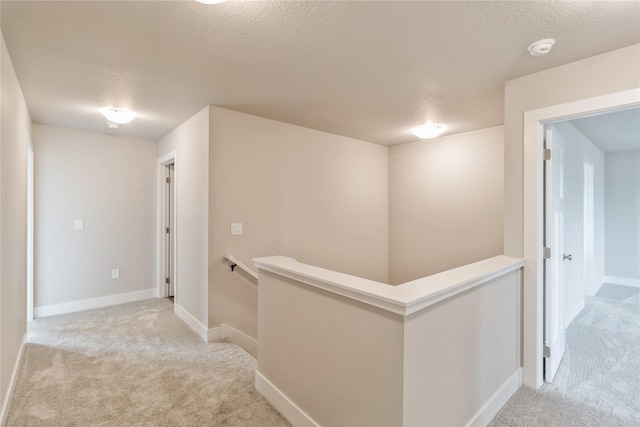 hallway with baseboards, carpet flooring, a textured ceiling, and an upstairs landing