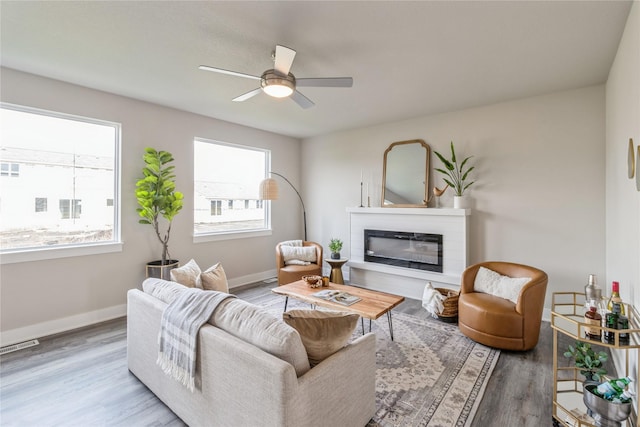 living area featuring visible vents, a glass covered fireplace, wood finished floors, baseboards, and ceiling fan