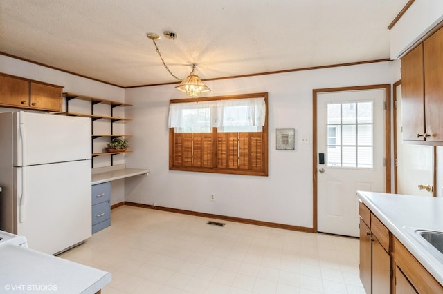 kitchen featuring built in study area, light countertops, freestanding refrigerator, and visible vents