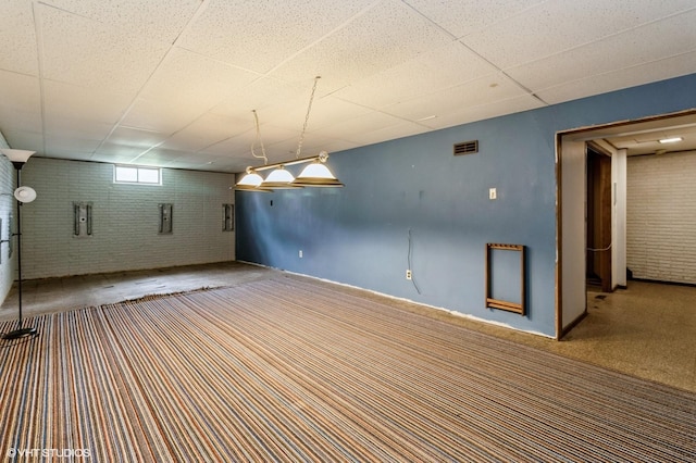 below grade area featuring visible vents, carpet flooring, a drop ceiling, and brick wall