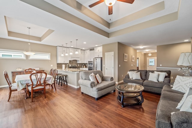 living room with a ceiling fan, baseboards, wood finished floors, and a raised ceiling