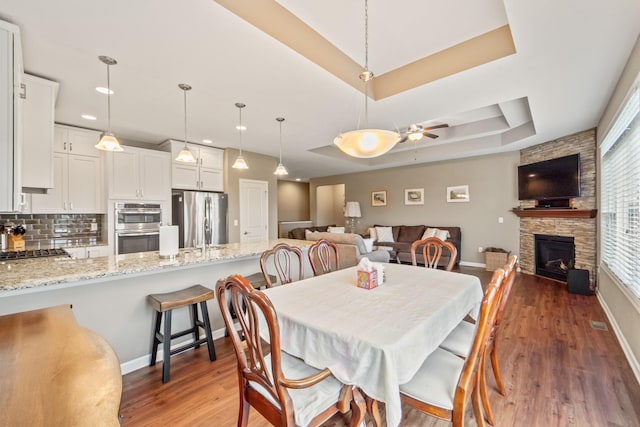 dining space with a fireplace, ceiling fan, baseboards, and wood finished floors