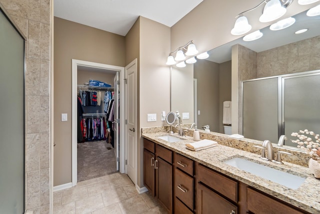 full bathroom with a sink, a walk in closet, a stall shower, and double vanity