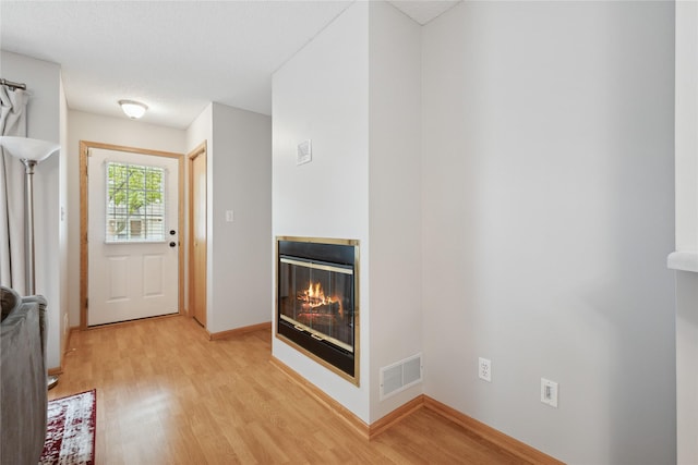 doorway featuring a textured ceiling, visible vents, baseboards, a glass covered fireplace, and light wood-style flooring