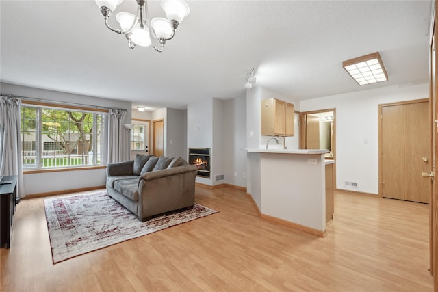 living area featuring visible vents, a glass covered fireplace, baseboards, light wood-type flooring, and a chandelier