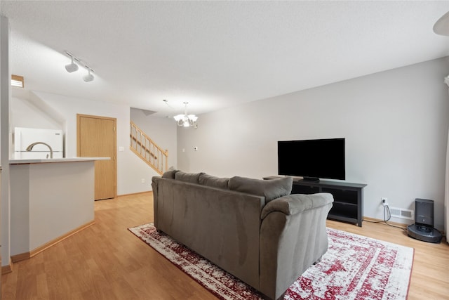 living area with track lighting, stairs, baseboards, a chandelier, and light wood finished floors