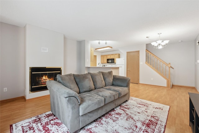 living room with stairway, an inviting chandelier, a glass covered fireplace, and light wood finished floors