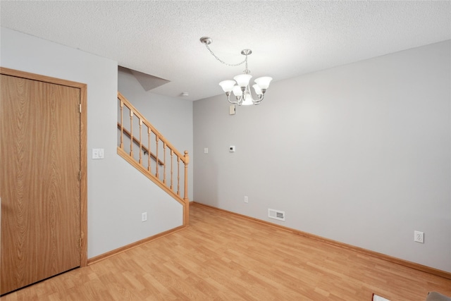 unfurnished room featuring an inviting chandelier, baseboards, wood finished floors, and stairway